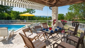 A covered outdoor area with a pool, lounge chairs, a table with cups, and a stone pillar.