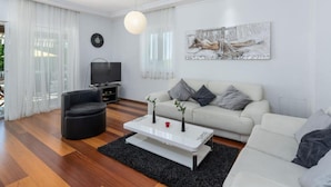 A modern living room with a sofa, a black armchair, a coffee table, a TV, and a painting on the wall.