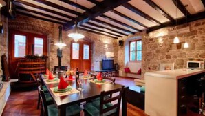 Interior rústico com vigas aparentes, paredes de pedra, área de jantar com mesa posta para quatro e uma cozinha compacta.
