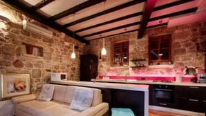 Uma sala de estar acolhedora com sofá, uma cozinha com parede de pedra e teto de madeira.