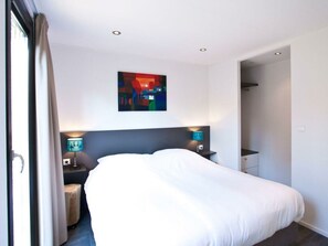 A hotel room with a large bed, two bedside tables with lamps, a colorful abstract painting on the wall, and a door leading to another room. - Holiday Home in Nijkerk With Terrace (Nijkerk)
