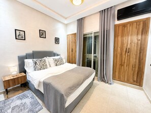 Quarto com cama, mesa de cabeceira, guarda-roupa de madeira e porta de correr de vidro.