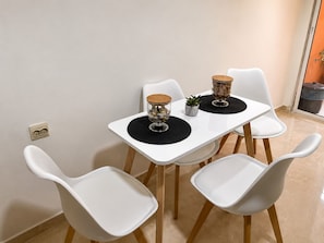 A dining table with four white chairs, two glass vases with wooden lids, and a small potted plant. - Modern 2-Bedroom Apartment in Central Gueliz Near Carré Eden (Marrakesh)