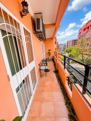 A balcony with a tiled floor, a small table with chairs, a potted plant, and a view of surrounding buildings. - Modern 2-Bedroom Apartment in Central Gueliz Near Carré Eden (Marrakesh)