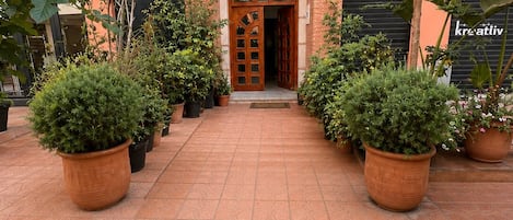A building entrance with a large wooden door, potted plants, and a sign in Arabic.