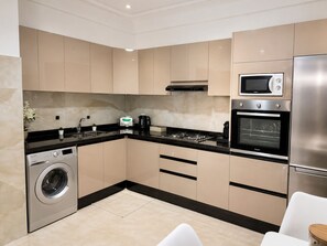 A modern kitchen with built-in appliances, a washing machine, and a dining area with a white chair. - Modern 2-Bedroom Apartment in Central Gueliz Near Carré Eden (Marrakesh)