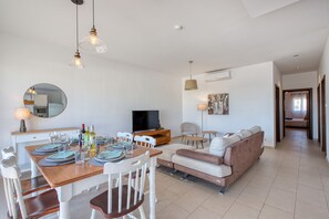 Ein modernes Wohnzimmer mit Essbereich, einer Couch, einem Fernseher und einem Spiegel.