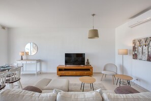 Ein modernes Wohnzimmer mit Fernseher, einer Couch, einem Esstisch, Stühlen und Bildern an der Wand.