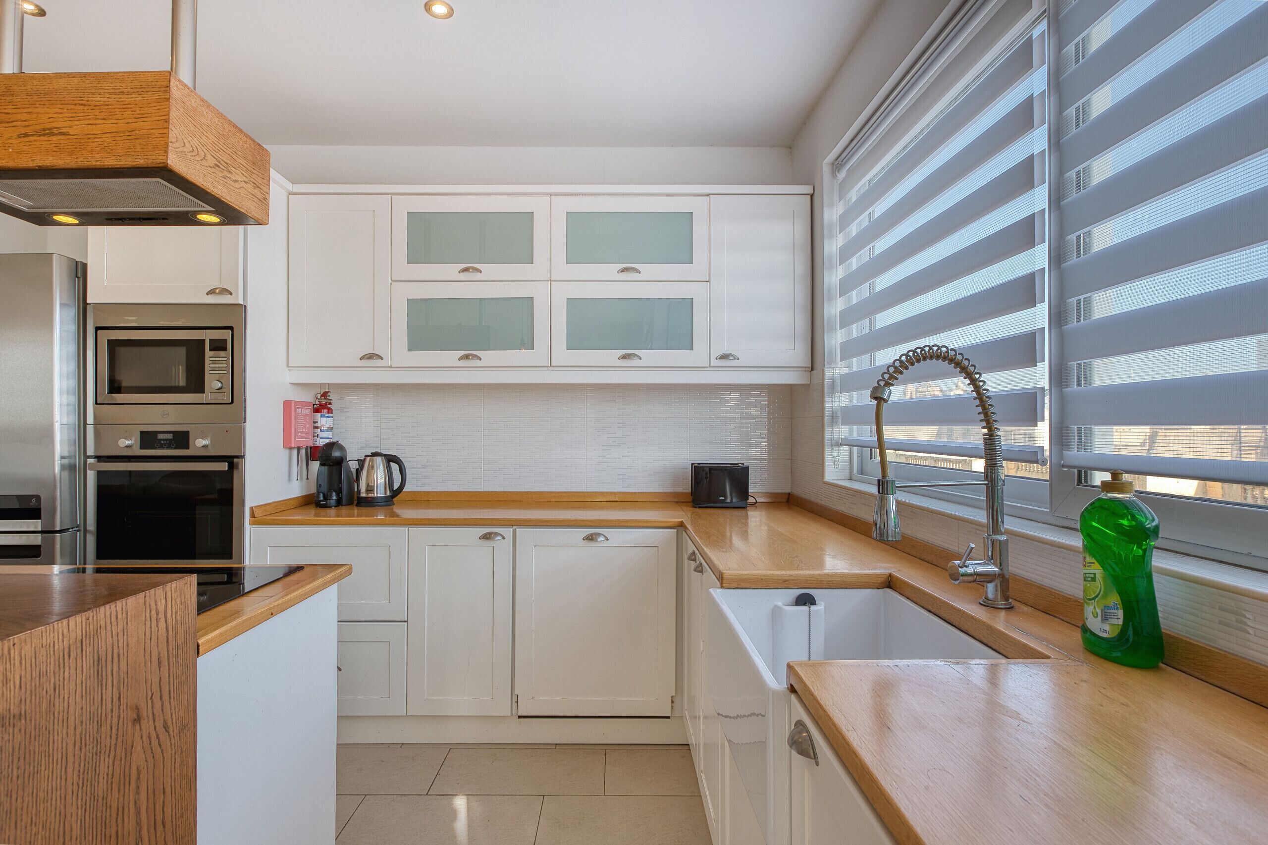 Una cocina moderna con armarios blancos, un microondas, un horno, un lavabo con grifo y una ventana con persianas.