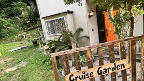 A wooden sign with 'Cruise Garden' written on it, a white building with a metal gate, and a small garden area with grass and plants.