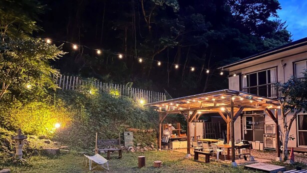 A covered outdoor seating area with string lights, a wooden pergola, and a small garden with a bench and a decorative lantern.