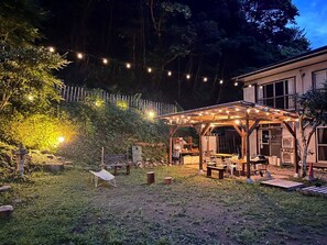 Een overdekt terras met lichtslingers, een houten pergola en een kleine tuin met een bankje en een decoratieve lantaarn.