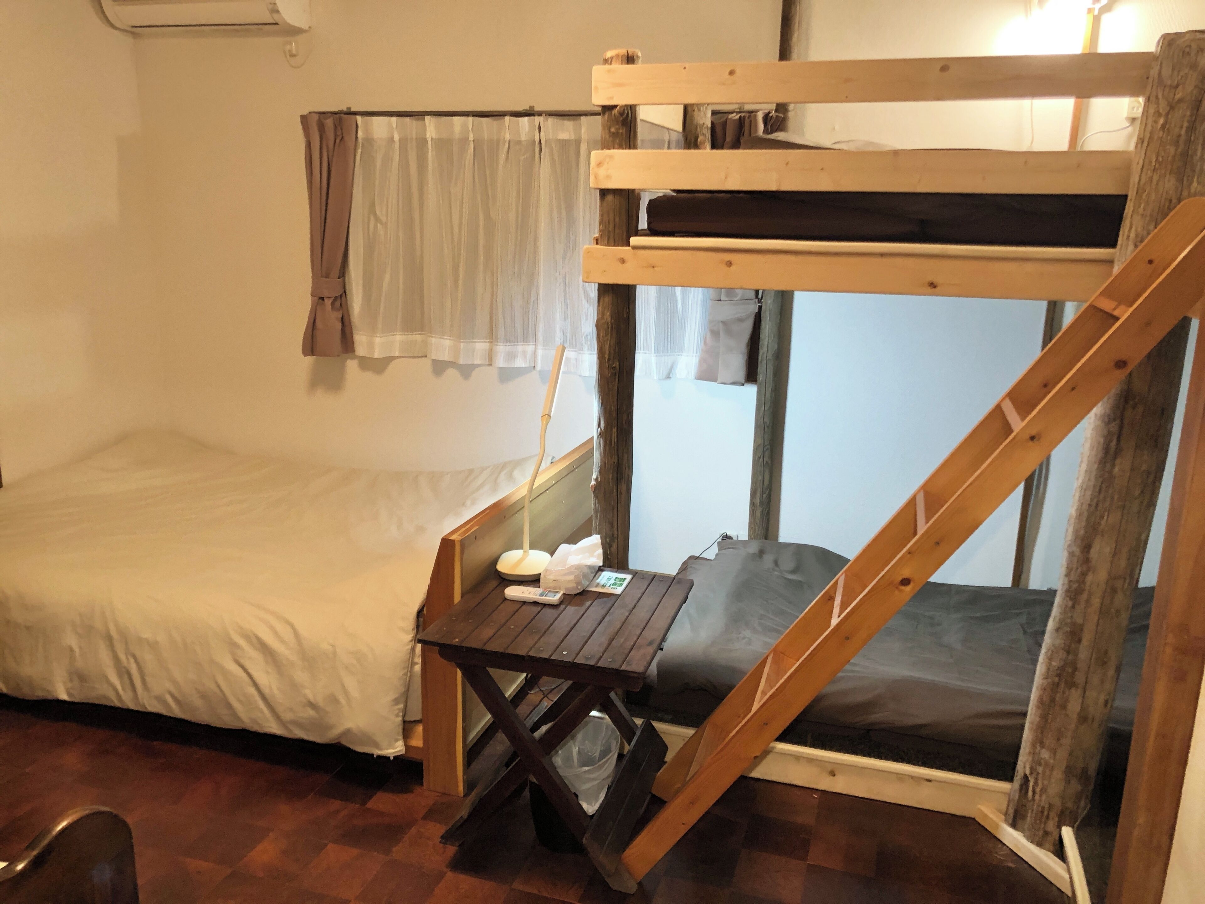 A bunk bed room with a small table, a remote control, and a plastic bag on the floor.