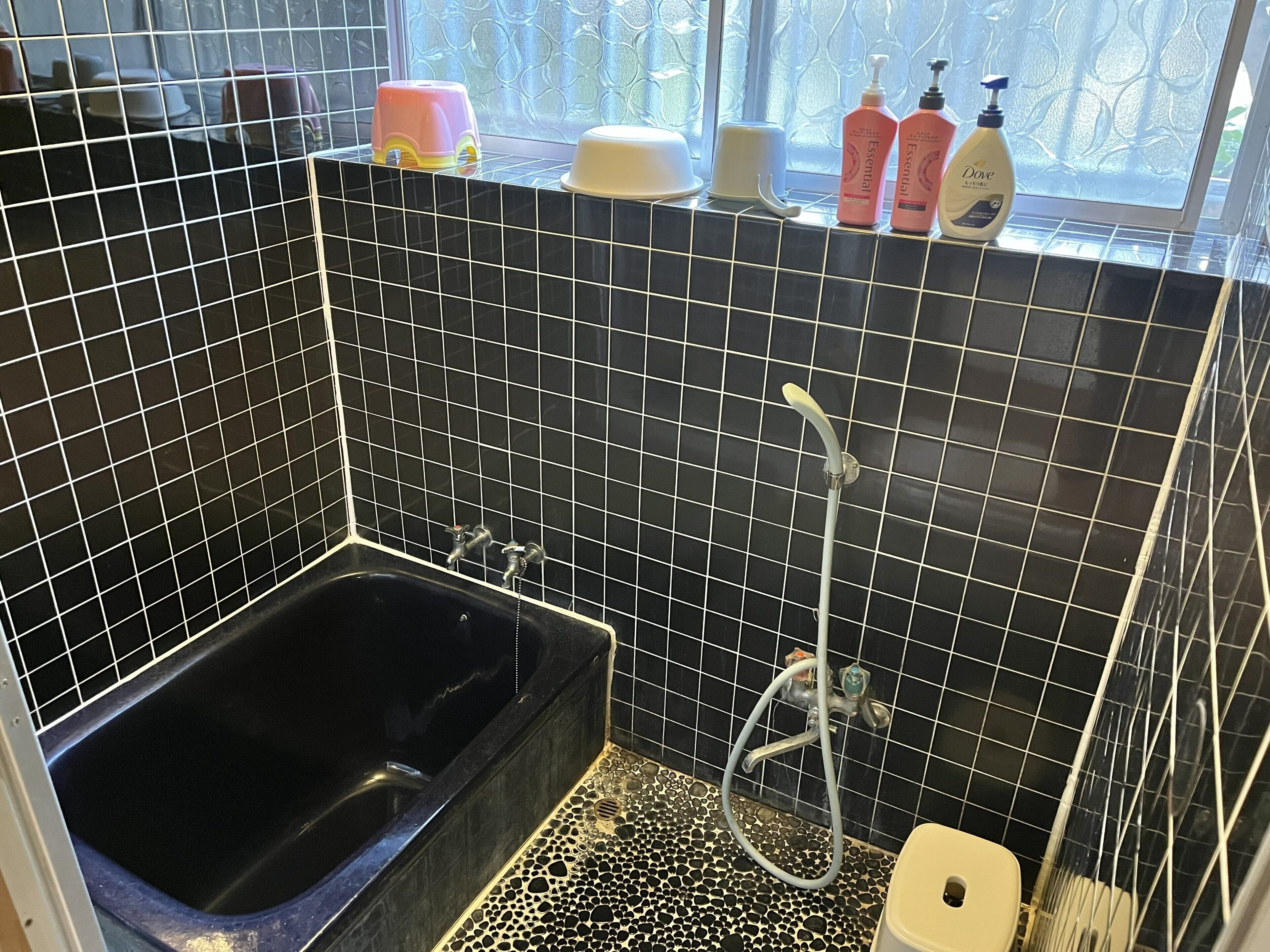 A bathroom with a black tiled wall, a bathtub, a shower, and toiletries on the windowsill.