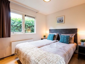 A double bed with a textured duvet, a window with curtains, a bedside table with a lamp, and a framed picture on the wall. - Holiday Home for 5 People (Noordwijk)