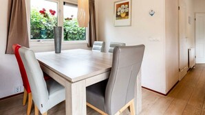 A dining area with a table, chairs, a vase with flowers, and a window with curtains. - Holiday Home for 5 People (Noordwijk)