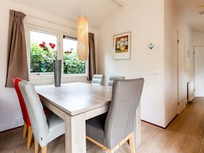 A dining area with a table, chairs, a vase with flowers, and a window with curtains. - Holiday Home for 5 People (Noordwijk)