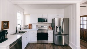 A kitchen with white cabinetry, stainless steel appliances, a wooden floor, and a window.