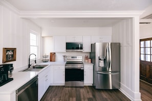 Una cocina con armarios blancos, electrodomésticos de acero inoxidable, piso de madera y una ventana.