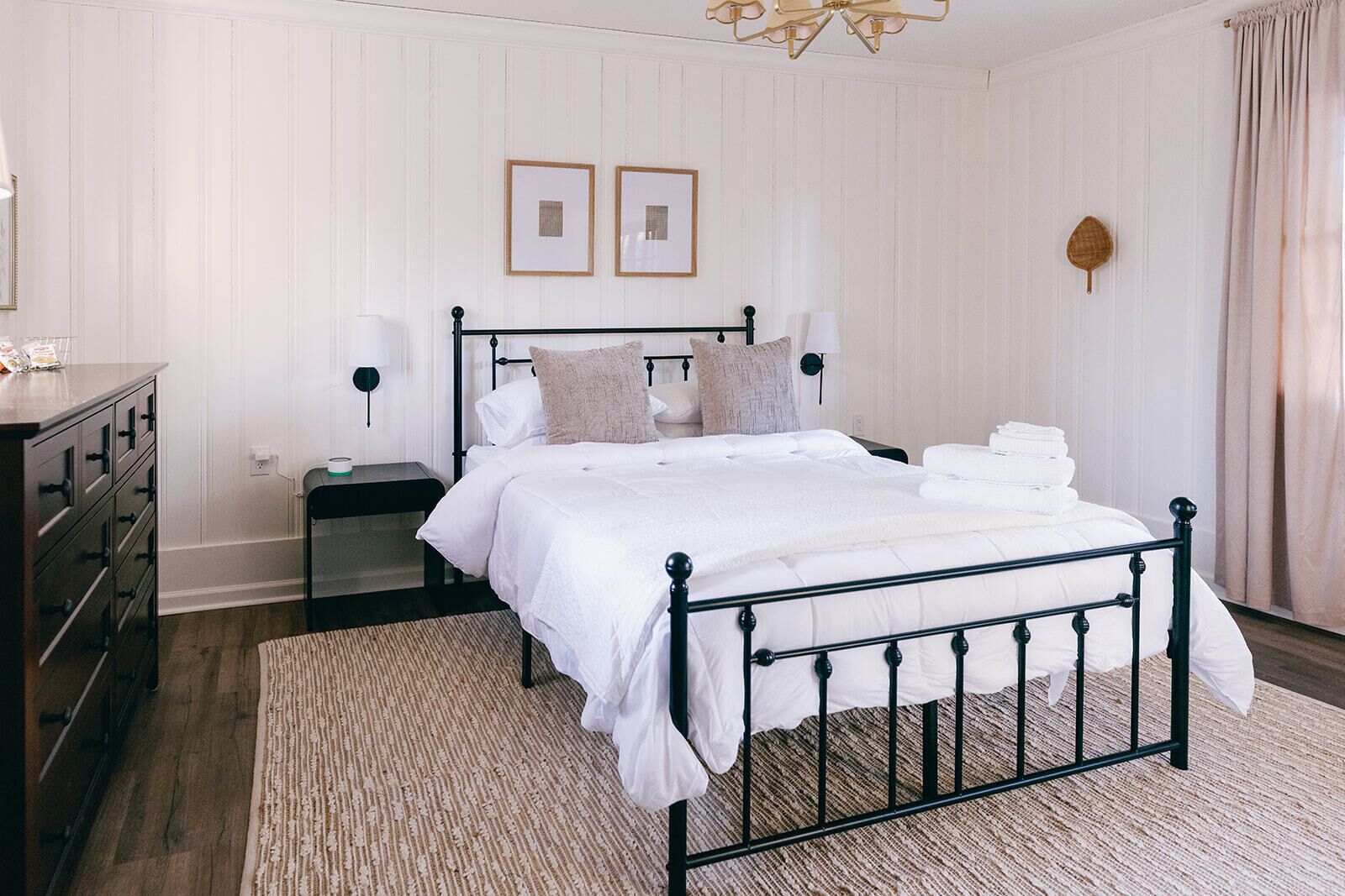 Un dormitorio ordenado con cama, mesitas de noche, cómoda y lámpara colgante.
