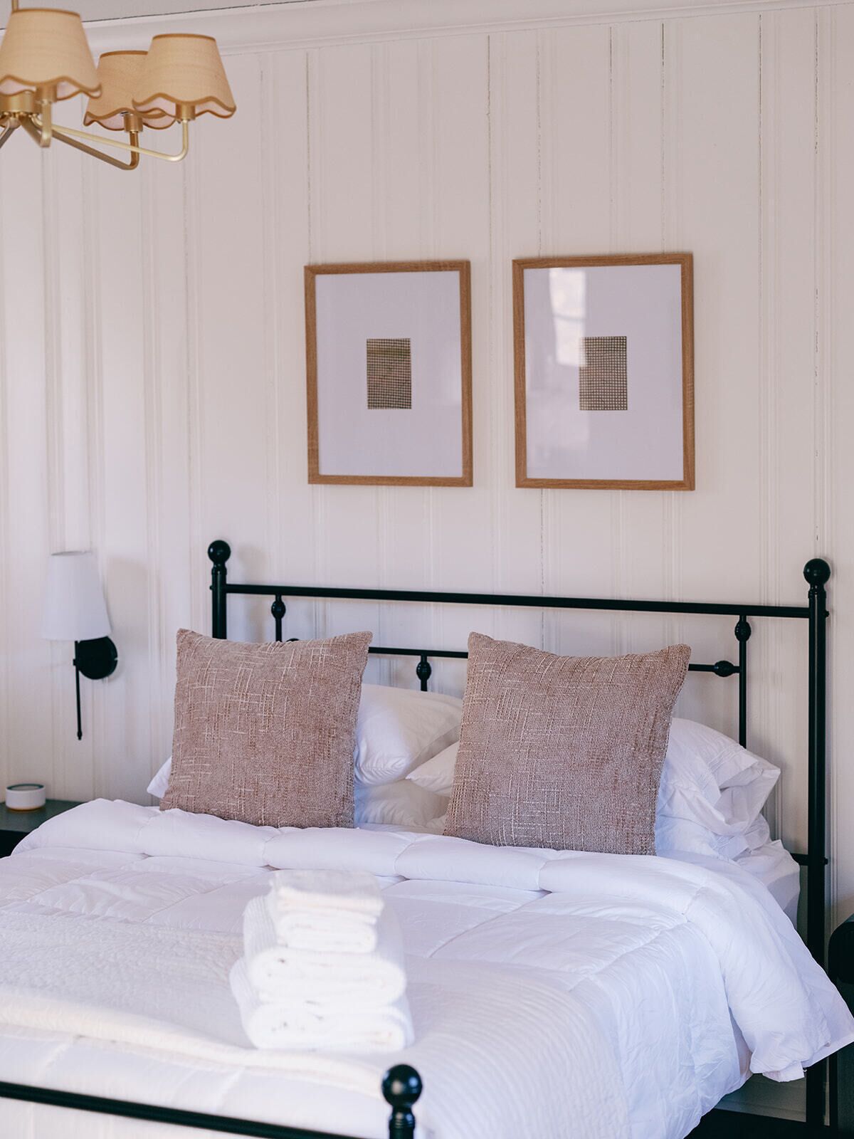 A neatly made bed with white bedding and two pillows, a bedside lamp, and two framed pictures on the wall.