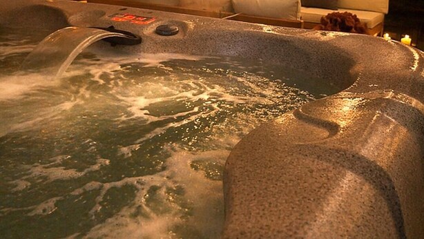A hot tub with a wooden deck, a sofa, and string lights.