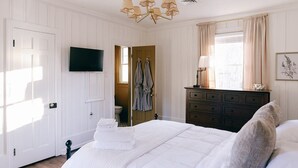 A bedroom with a bed, a dresser, a TV, and a window with curtains.