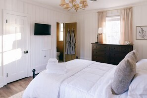 Un dormitorio con cama, cómoda, televisor y ventana con cortinas.