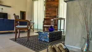 Un salon comprenant un canapé, deux fauteuils en bois, un tapis à motifs, une boîte décorative bleue et un vase avec des branches.