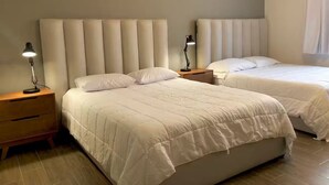 Une chambre d’hôtel avec deux lits, une table de chevet en bois, une lampe et une tête de lit fixée au mur.