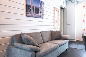 A grey sofa with cushions, a framed picture on the wall, and a door leading to another room. - Two-Floor Apartment in Levi Center (Kittilä)