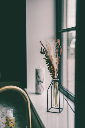 Eine Vase mit getrockneten Pflanzen auf einem Fensterbrett, eine Kerze und eine Lotionflasche.