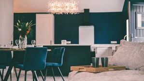 Una sala moderna con un sofá, una zona de comedor con sillas, una araña y un florero con flores.