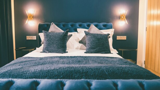 Un dormitorio con cabecera capitonada, dos mesitas de noche e iluminación fijada a la pared.