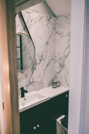 Ein Badezimmer mit Marmorwand, Waschbecken, Spiegel und Toilette.