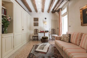 Ein Zimmer mit einem gestreiften Sofa, einem Glastisch mit einem Buch, einer Holzbalkendecke und einer Wandlampe.
