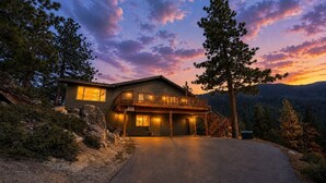 A two-story lodge with a balcony, surrounded by trees and a mountain backdrop.
