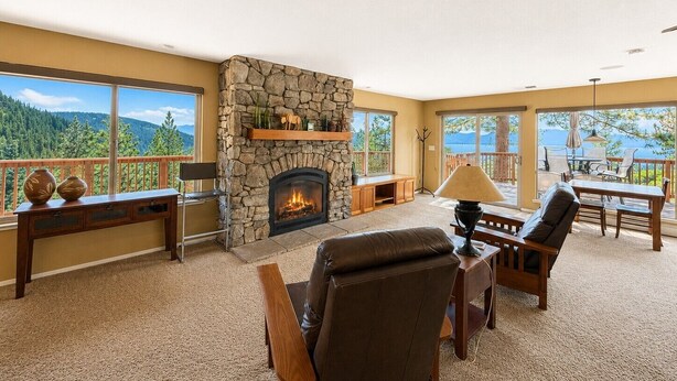 A living room with a stone fireplace, large windows, and a view of the mountains.