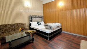 Een slaapkamer met een bed, een bank, een glazen salontafel en houten lambrisering.