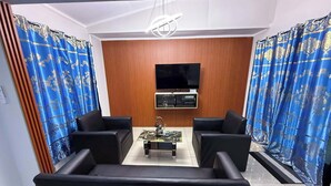 Ein modernes Wohnzimmer mit einem Flachbildfernseher, zwei schwarzen Sofas, einem Couchtisch und blau gemusterten Vorhängen.