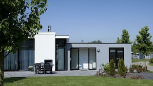 A modern building with a flat roof, large windows, and a patio area with chairs. - Cube Exclusive 4 (Velsen-Zuid)
