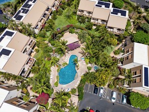 Luftaufnahme eines Resorts mit mehreren Gebäuden, einem zentralen Schwimmbecken und umliegender Bepflanzung.