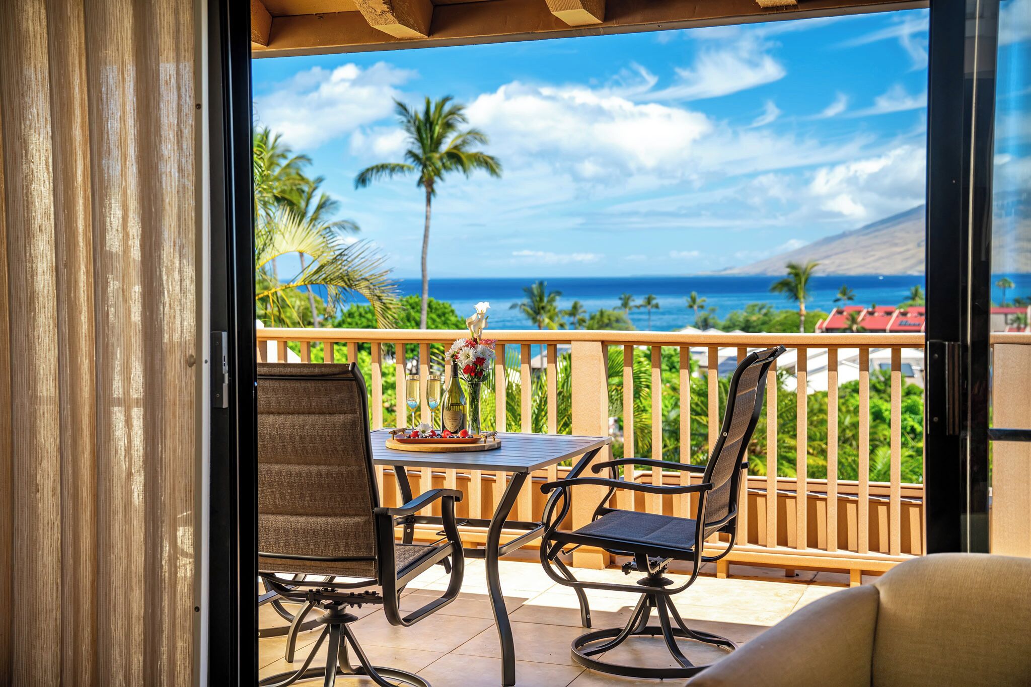 Een balkon met een tafel en stoelen, uitzicht op de oceaan en palmbomen.