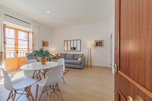 Een moderne woonkamer met een grijze bank, witte stoelen, een ronde tafel en een houten vloer.