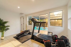 Ein Heimfitnessraum mit Laufband, Hanteln und einem großen Fenster mit Blick auf einen Swimmingpool.
