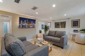 Ein modernes Wohnzimmer mit einem grauen Sofa, einem Glastisch und einem Stadtbild an der Wand.