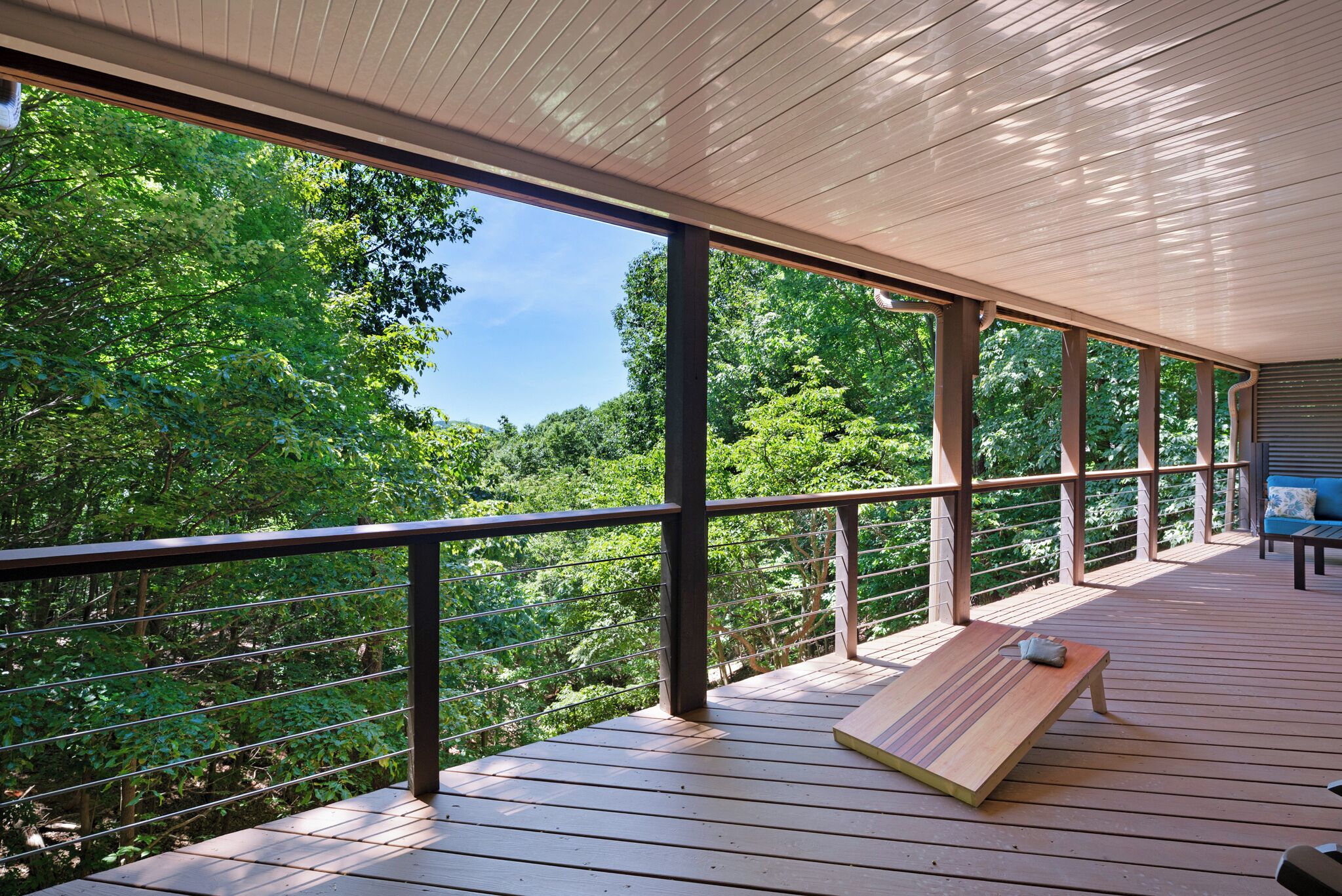 A wooden deck with a bench, metal railing, and a view of dense greenery.