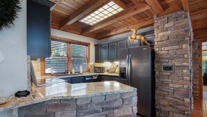 A kitchen with a stone accent wall, a black refrigerator, and wooden ceiling beams. - Chalet Lumiere - Big Canoe, GA (Jasper)