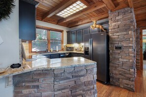 A kitchen with a stone accent wall, a black refrigerator, and wooden ceiling beams. - Chalet Lumiere - Big Canoe, GA (Jasper)