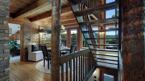 A wooden interior with a staircase, a dining area with chairs and a table, and a view through large windows. - Chalet Lumiere - Big Canoe, GA (Jasper)